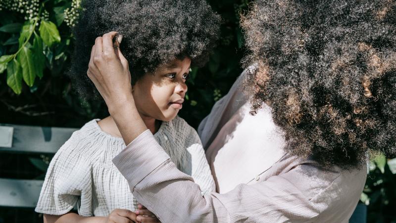 A mother holds her young child's face gently in a sunlit garden.
