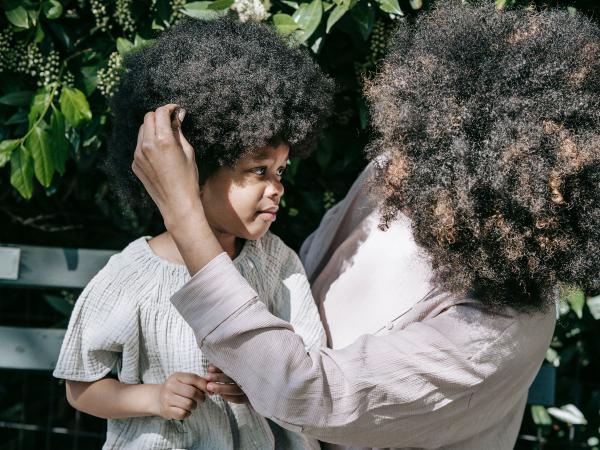 A mother holds her young child's face gently in a sunlit garden.