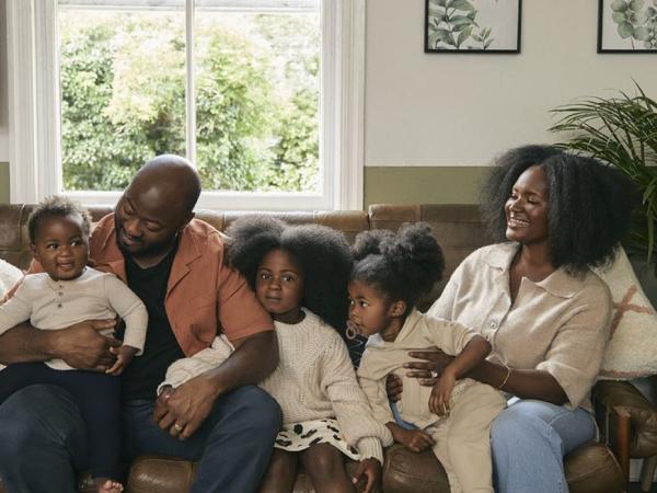 Parents sit on a sofa surrounded by their four young children